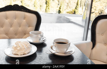 Deux tasses de café noir avec meringue sur une table en bois foncé texturé dans un café avec un décor classique. Close-up. Banque D'Images