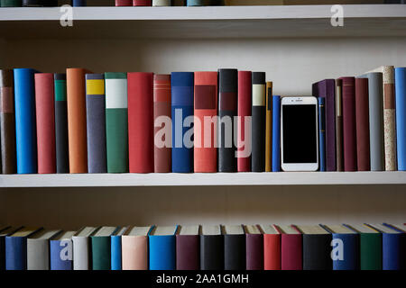 Bibliothèque précis avec un téléphone mobile debout entre les couvertures de livres colorés Banque D'Images