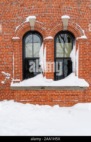 La neige s'entasse dans windows d'un vieux bâtiment en brique. Banque D'Images