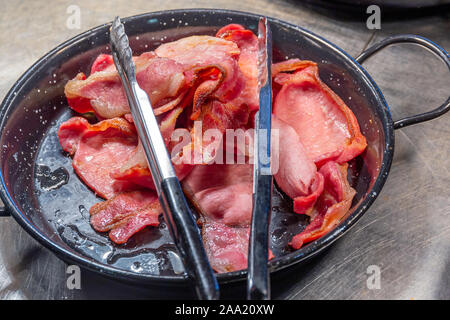 Pile de bacon cuit dans une poêle avec pinces pour le petit déjeuner buffet de l'hôtel Banque D'Images