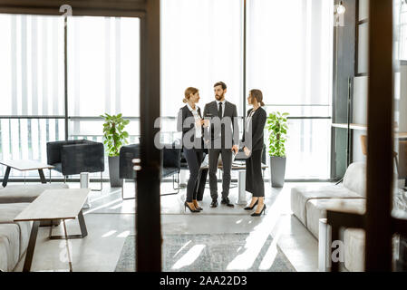 Les employés de l'institution financière, et dont certaines affaires, debout et parler dans le bureau de luxe. Voir à travers la porte Banque D'Images