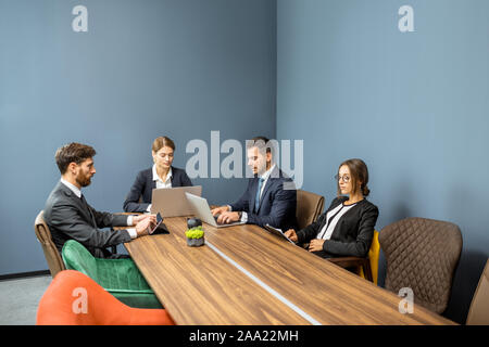 Groupe de gens d'affaires strictement vêtus de costumes de l'assise à la grande table au cours d'une conférence dans la salle de réunion Banque D'Images