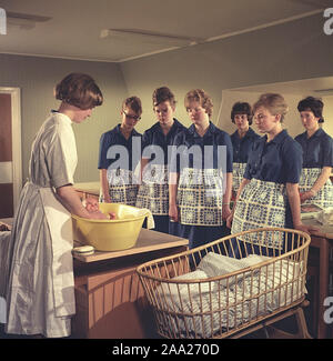 Apprendre à avoir un bébé dans les années 60. Une classe dans la façon de prendre soin d'un bébé. Un groupe de jeune femme regarde et écoute un professeur avec une poupée pour enfants. Suède 1960 Banque D'Images