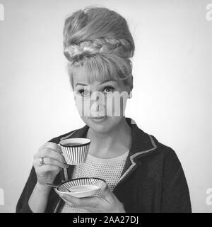 Café dans les années 1960. Une femme est de boire du café à partir d'un 1960 coffeecup avec un motif à rayures. Elle a ses cheveux dans la ruche typique hairstyle, dont les cheveux longs s'entasse sur le dessus de la tête et de donner une certaine ressemblance avec la forme d'une ruche traditionnelle. Suède 1962. Ref BV97-8 Banque D'Images