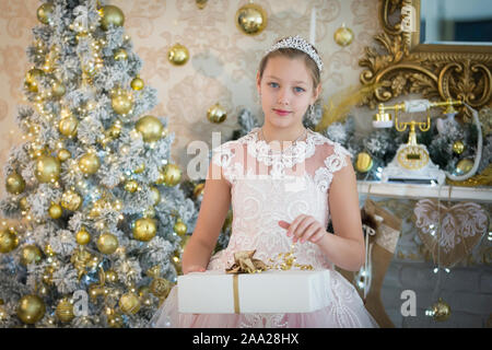 Fille élégante au Nouvel An des arbres avec un cadeau. Enfant à Noël. Portrait d'un adolescent dans un luxueux intérieur Noël riche. Banque D'Images