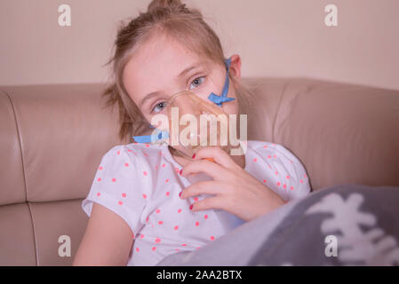 La petite fille ne l'inhalation à la maison.La jeune fille est assise à l'inhalation. L'enfant est malade et triste. La petite fille se sent mal. Banque D'Images