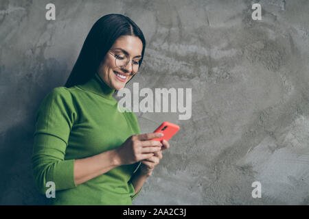Photo de cheerful pretty cute woman smiling toothily téléphone parcourant près de l'espace vide de couleur gris béton isolé mur d'arrière-plan Banque D'Images