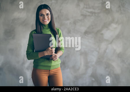 Photo de bonne humeur assez positive woman holding laptop avec mains smiling toothily isolé près de l'espace vide en arrière-plan en béton mur gris Banque D'Images