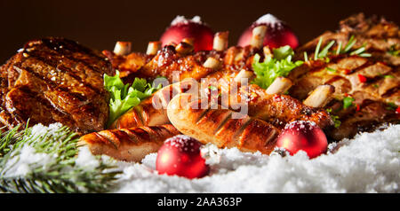 Panorama de la viande grillé épicé de Noël un barbecue avec des saucisses de porc steak de boeuf spare ribs et coloré de Noël rouge blanc décorations sur neige de l'hiver Banque D'Images