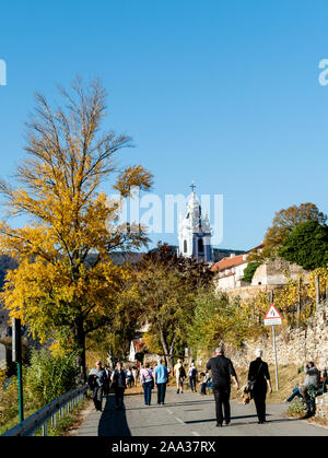 Les touristes à marcher le long de la Danube banque à Durnstein, l'Autriche, avec le monastère en arrière-plan Banque D'Images