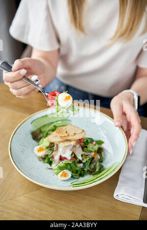 Femme mange avec salade Olivier, langue d'agneau concombre salé, oeuf de caille. Arrière-plan de table en bois. Restaurant Menu. Salade traditionnelle russe Banque D'Images