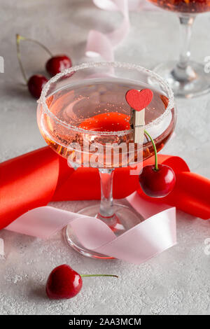 Le verre à champagne avec vin de fête sur rose sur fond gris avec des rubans de vacances Banque D'Images