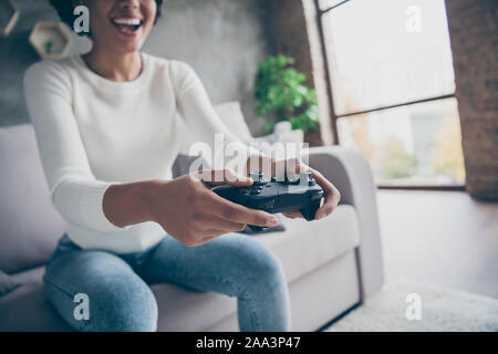 Photo recadrée de funny peau sombre dame jouant des jeux vidéo accro maintenez joystick moderne football match assis canapé confortable porter des jeans Pull décontracté Banque D'Images