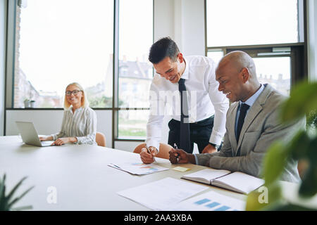 Deux smiling businessmen discussing paperwork avec un collègue dans un contexte au cours d'une réunion autour d'une table de conférence Banque D'Images