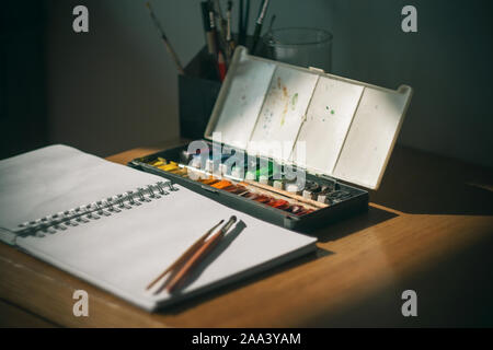 Le travail de l'artiste sur la table, où l'aquarelle, de croquis et de brosses se trouvent, est éclairé par un rayon de soleil qui traverse le darknes Banque D'Images