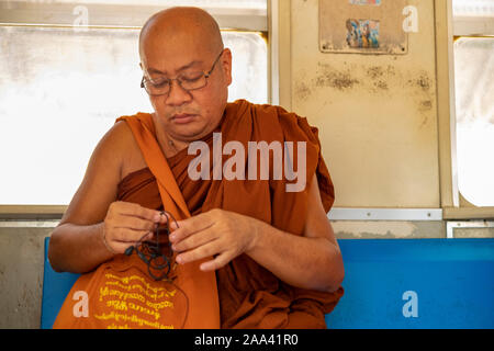 Un vieux moine bouddhiste dans une robe safran portant des lunettes vérifie son téléphone portable lors des trajets sur un train local dans le centre de Yangon, Myanmar (Birmanie) Banque D'Images