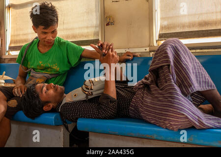 Deux jeunes vendeurs birmans prennent une pause et vérifier un téléphone mobile alors que sur un train local sur la route circulaire autour de Yangon, Myanmar (Birmanie) Banque D'Images