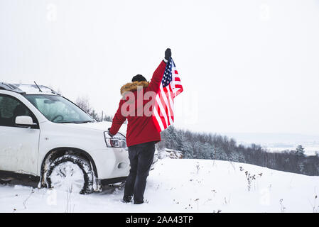 Homme debout sur le sommet de la colline, USA drapeau dans ses mains près de voiture suv à la belle vue d'hiver