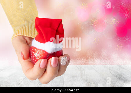 Main de femme magnifique avec noël nail design. La main avec rose manucure ongles élégant tenant une boule de décoration de Noël rouge avec un Santa Claus hat. Banque D'Images