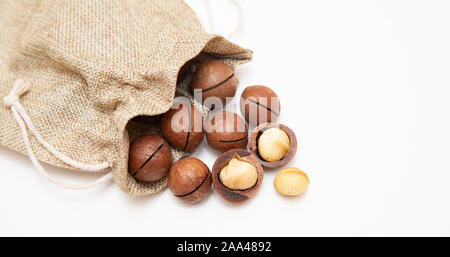 Pile de macadamia décortiquées ouvert et coquilles dans un sac de toile sur fond blanc, vue du dessus. Banque D'Images