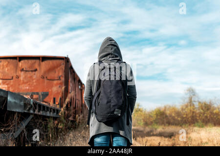 Sac à dos femme sans-abri à se retirer du monde, vue arrière de la marche chez les wagons de train abandonné et obsolètes railroad track Banque D'Images