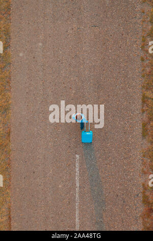 Woman pulling suitcase voyage assurance sur la route en automne coucher du soleil, high angle view de drone pov Banque D'Images