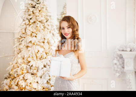 Belle jeune femme holding Christmas présents dans les mains sur l'arrière-plan flou floue. Nouveau concept de l'an. Banque D'Images