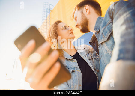 Famille en supermarché. Jeune femme utilise le téléphone mobile pour choisir des produits et des choses, l'homme détient le panier. Banque D'Images