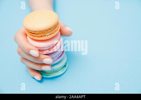 Fille main beauté manucure avec des macarons couleur prise sur fond bleu. Banque D'Images