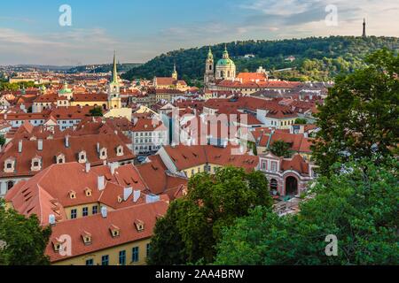 Prague, République tchèque - 20 juillet 2019 - Vue sur les toits rouges, paysage urbain avec les églises et la colline de Petrin lointain avec une tour. Soirée bleu ciel avec des nuages. Banque D'Images