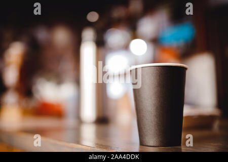 Arrière-plan flou paper tasse de café se tient sur comptoir de boutique, lumière sombre bokeh. Banque D'Images