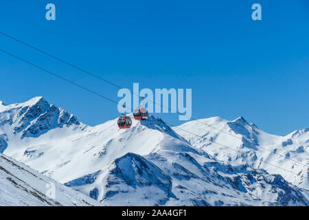 Deux gondoles qui montent et descendent au-dessus de la neige caped montagnes. Déménagement les gondoles sont suspendus sur des cordes épaisses très élevé. Dans le dos il y a des grands Alpes. Banque D'Images