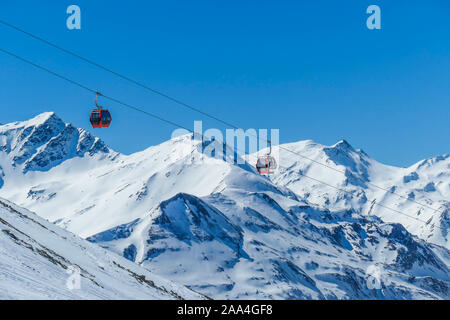 Deux gondoles qui montent et descendent au-dessus de la neige caped montagnes. Déménagement les gondoles sont suspendus sur des cordes épaisses très élevé. Dans le dos il y a des grands Alpes. Banque D'Images