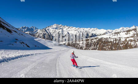 Un snowboarder en descendant la pente à Heiligenblut, Autriche. Des pistes parfaitement entretenues. De hautes montagnes entourant l'homme portant un pantalon jaune et Banque D'Images