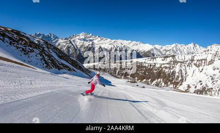 Un snowboarder en descendant la pente à Heiligenblut, Autriche. Des pistes parfaitement entretenues. De hautes montagnes entourant l'homme portant un pantalon jaune et Banque D'Images