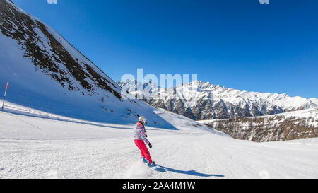 Un snowboarder en descendant la pente à Heiligenblut, Autriche. Des pistes parfaitement entretenues. De hautes montagnes entourant l'homme portant un pantalon jaune et Banque D'Images