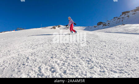 Un snowboarder en descendant la pente à Heiligenblut, Autriche. Des pistes parfaitement entretenues. De hautes montagnes entourant l'homme portant un pantalon jaune et Banque D'Images