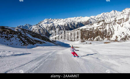 Un snowboarder en descendant la pente à Heiligenblut, Autriche. Des pistes parfaitement entretenues. De hautes montagnes entourant l'homme portant un pantalon jaune et Banque D'Images
