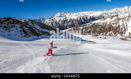 Un snowboarder en descendant la pente à Heiligenblut, Autriche. Des pistes parfaitement entretenues. De hautes montagnes entourant l'homme portant un pantalon jaune et Banque D'Images