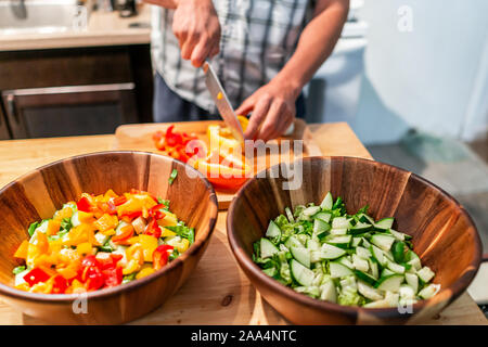 Man chopping vegetables on cutting board table avec deux grands bols de légumes salade végétalienne avec poivrons orange rouge dans la cuisine Banque D'Images