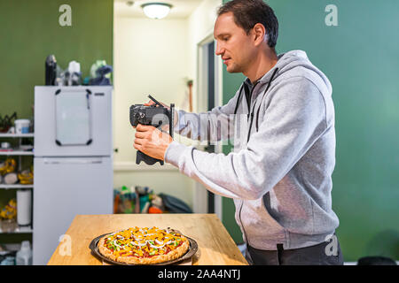 Photographe professionnel homme dessus plat en photo avec l'appareil photo de pizza cuite fait maison avec une sauce tomate et fromage cheddar vegan orange garnitures Banque D'Images