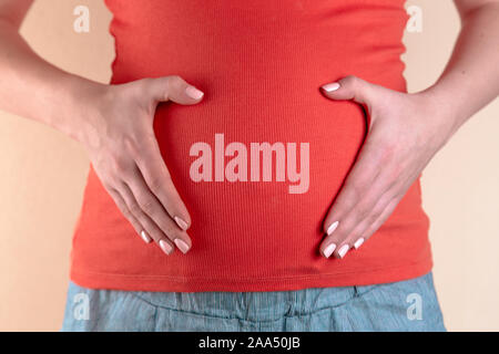 Une vue rapprochée du ventre d'une femme enceinte dans un T-shirt rouge, qui tient son ventre avec ses mains formant une forme de coeur. Le concept de l'amour et Banque D'Images