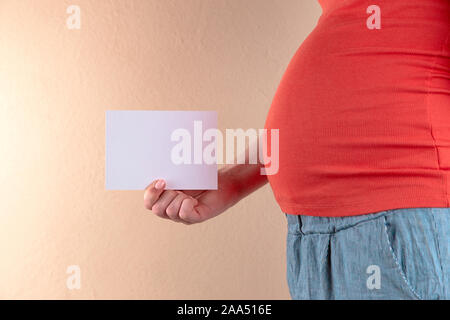 Une vue rapprochée du ventre d'une femme enceinte dans un T-shirt rouge c'est la tenue d'une feuille de papier vide Banque D'Images