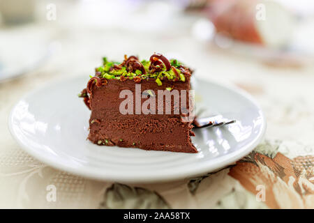 Libre composé de couches de chocolat noir pistache gâteau végétalien premières tranche sur plaque blanche avec des copeaux de chocolat et de noix pièces vert texture Banque D'Images