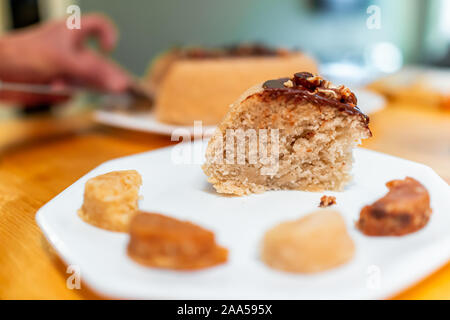 Une tranche de gâteau fait maison vanille jaune avec glaçage au chocolat et noix de coco macarons sur table et fond flou de part le tranchage dessert Banque D'Images