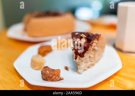 Gros plan d'une tranche de gâteau fait maison vanille jaune avec glaçage au chocolat et noix de coco macarons sur table et fond flou de dessert Banque D'Images