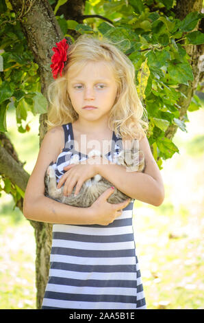 Belle blonde girl in blue dotted dress holding d'armes peu chat domestique Banque D'Images