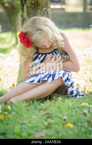 Belle blonde girl in blue dotted dress holding d'armes peu chat domestique Banque D'Images