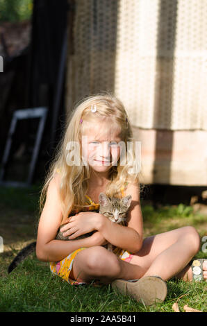 Belle blonde girl in blue dotted dress holding d'armes peu chat domestique Banque D'Images