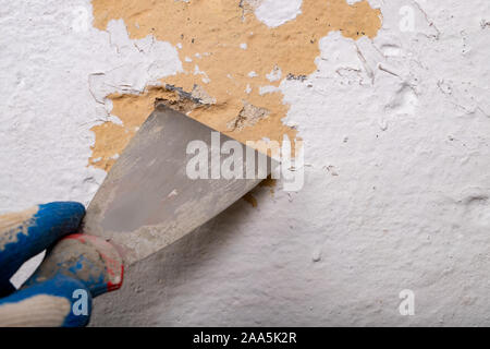 Enlever de la vieille peinture du mur avec une spatule métallique. Petits travaux de peinture à la maison. Fond clair. Banque D'Images